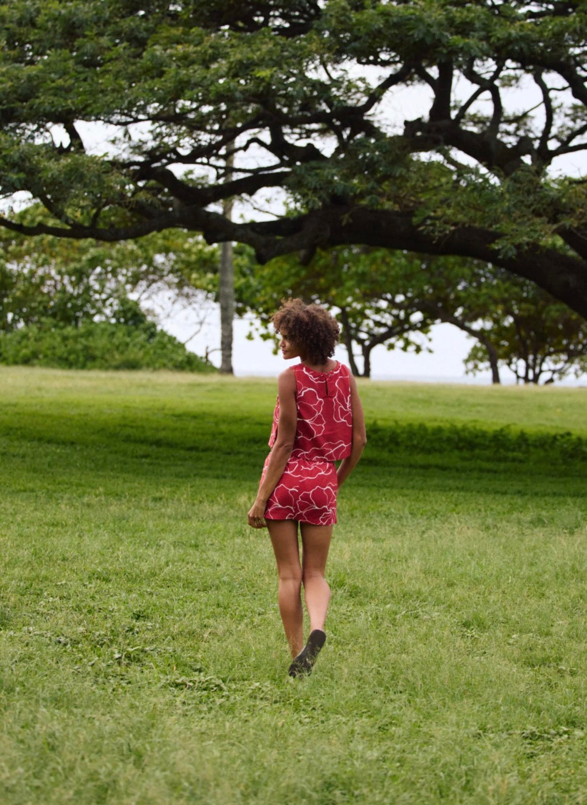 Person in a red dress walking on grass with trees in the background