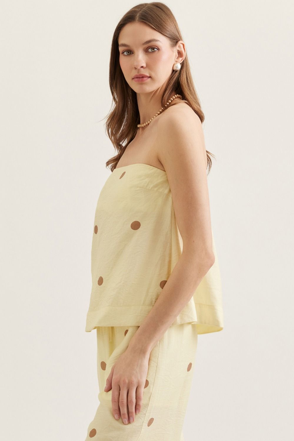 Woman wearing a light yellow strapless top with polka dots on a plain background
