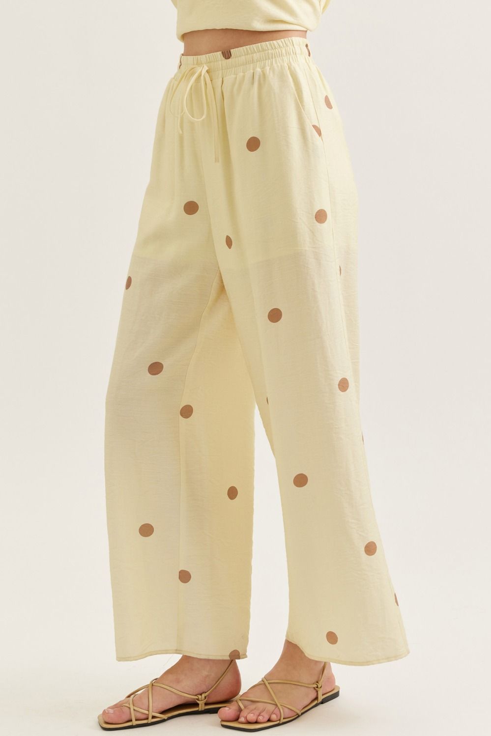 Beige pants with brown polka dots worn by a person on a white background