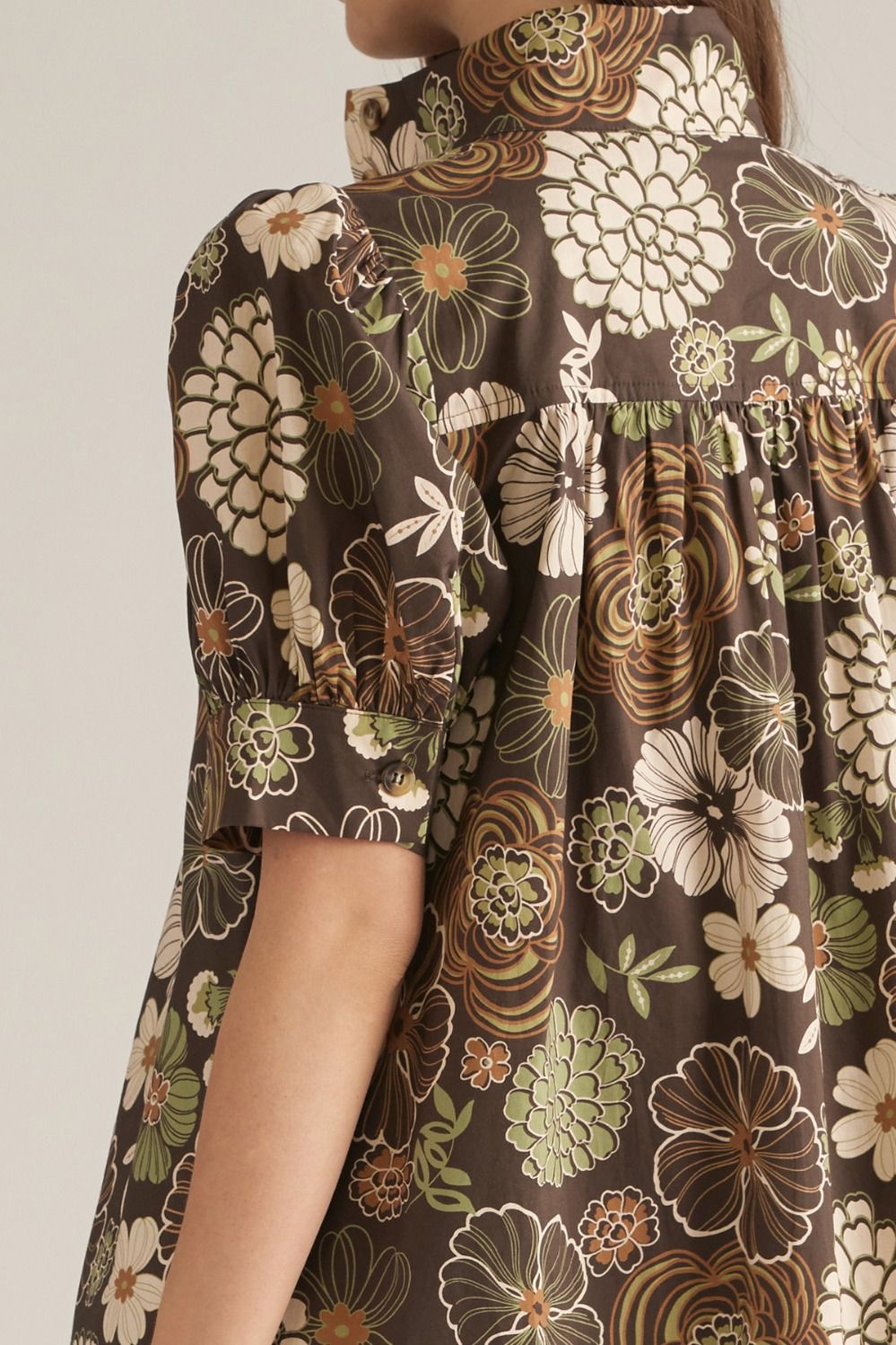Close-up of a person wearing a brown short-sleeve blouse with a retro floral print in beige, olive green, and brown.