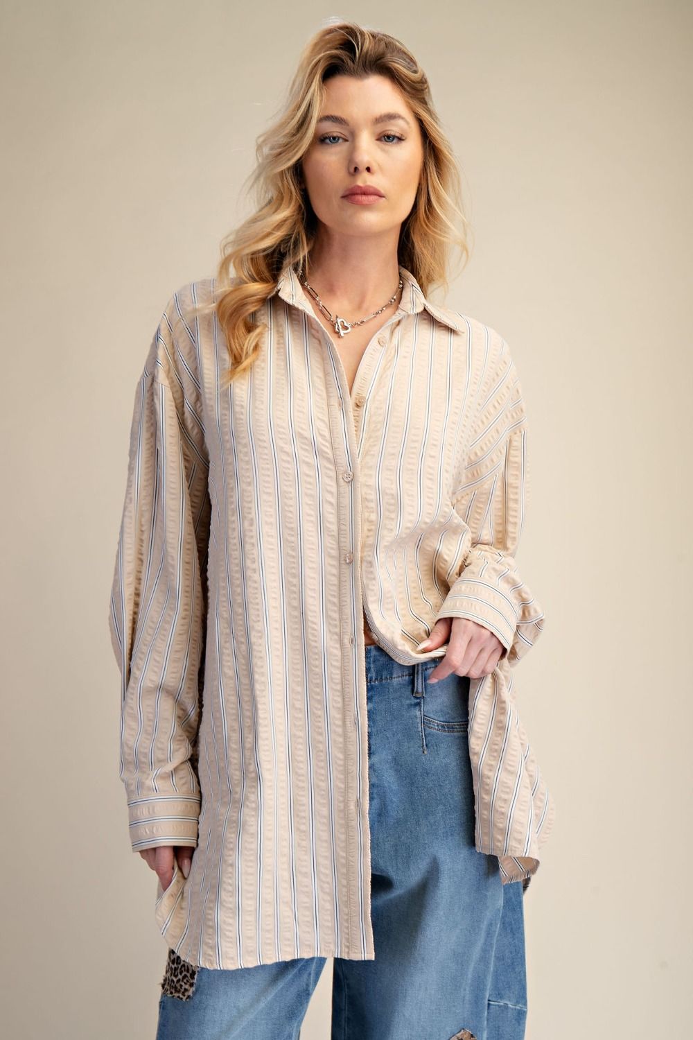 Woman wearing a long, striped shirt over a blouse with blue jeans against a beige background