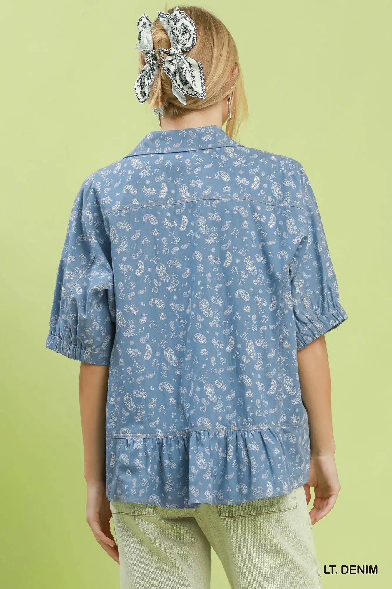 Person wearing a light denim shirt with a subtle pattern on a green background