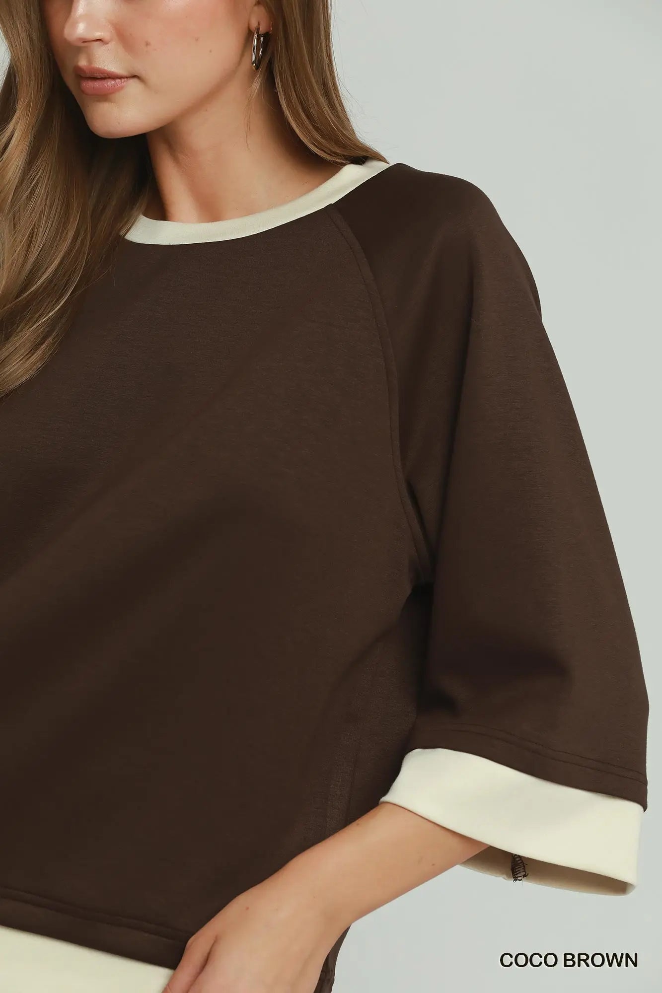 Brown sweater with white trim worn by a person on a light gray background