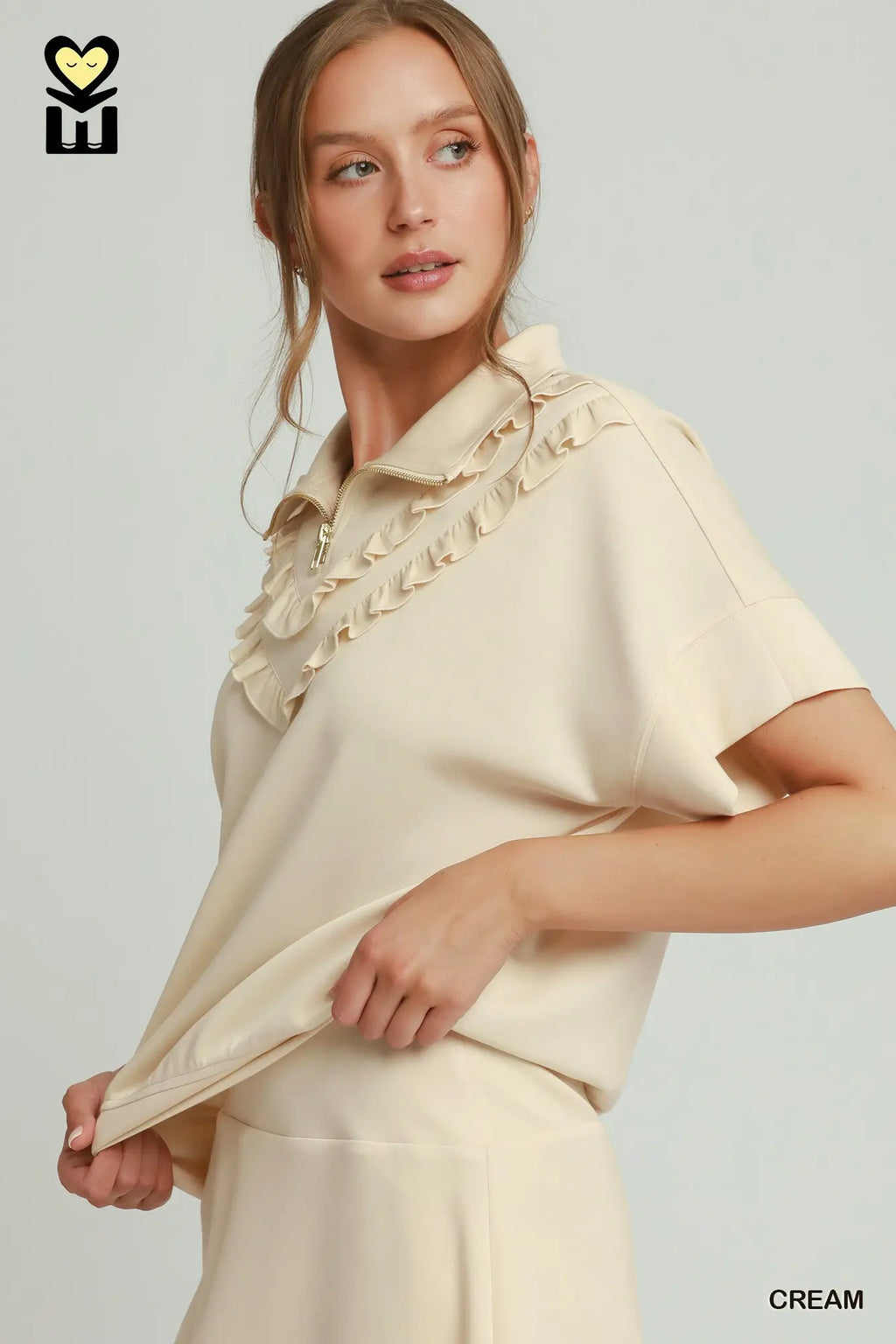 Woman wearing a cream blouse with ruffled details on a light gray background