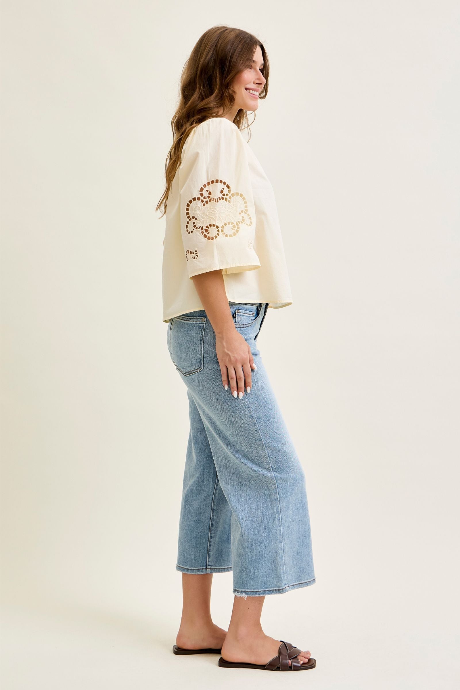 Woman wearing a cream top with a floral design and light blue jeans on a white background