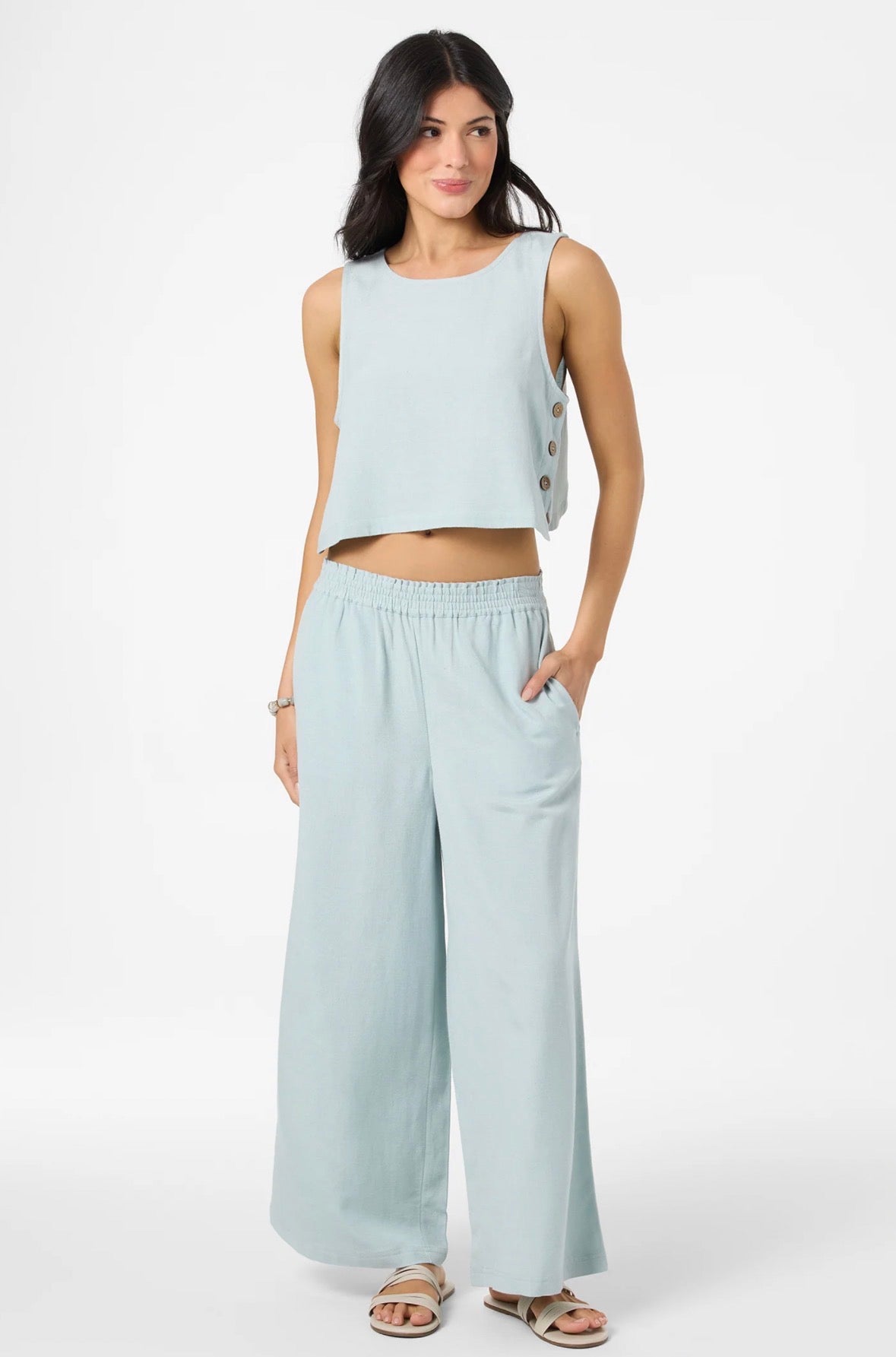 Woman wearing a light blue sleeveless top and wide-leg pants on a white background