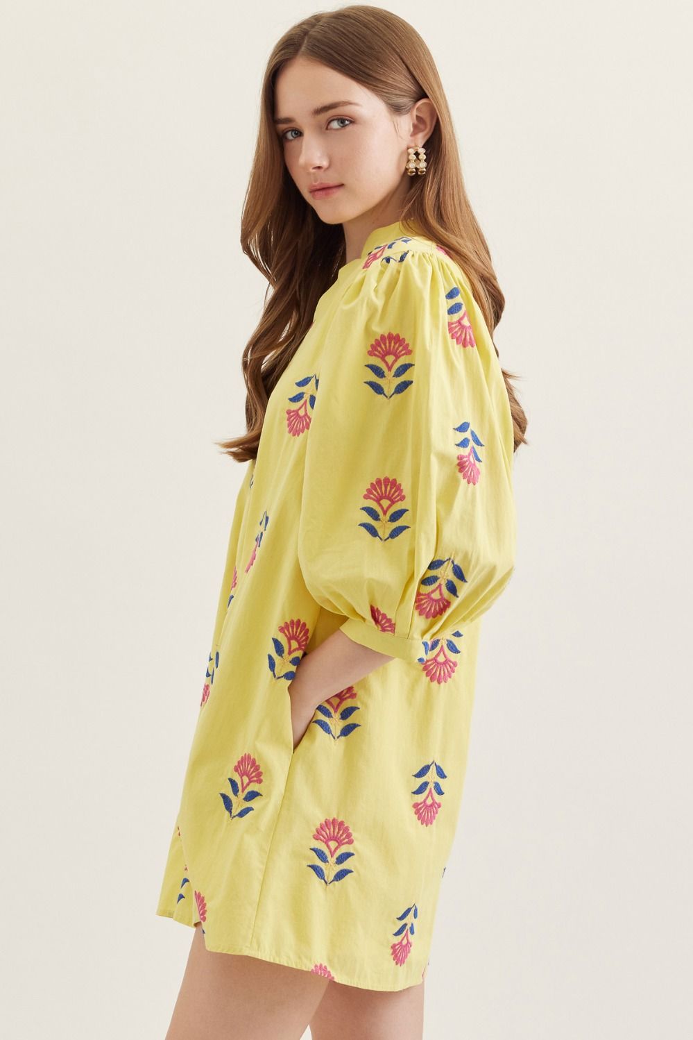 Woman wearing a yellow dress with floral patterns on a plain background
