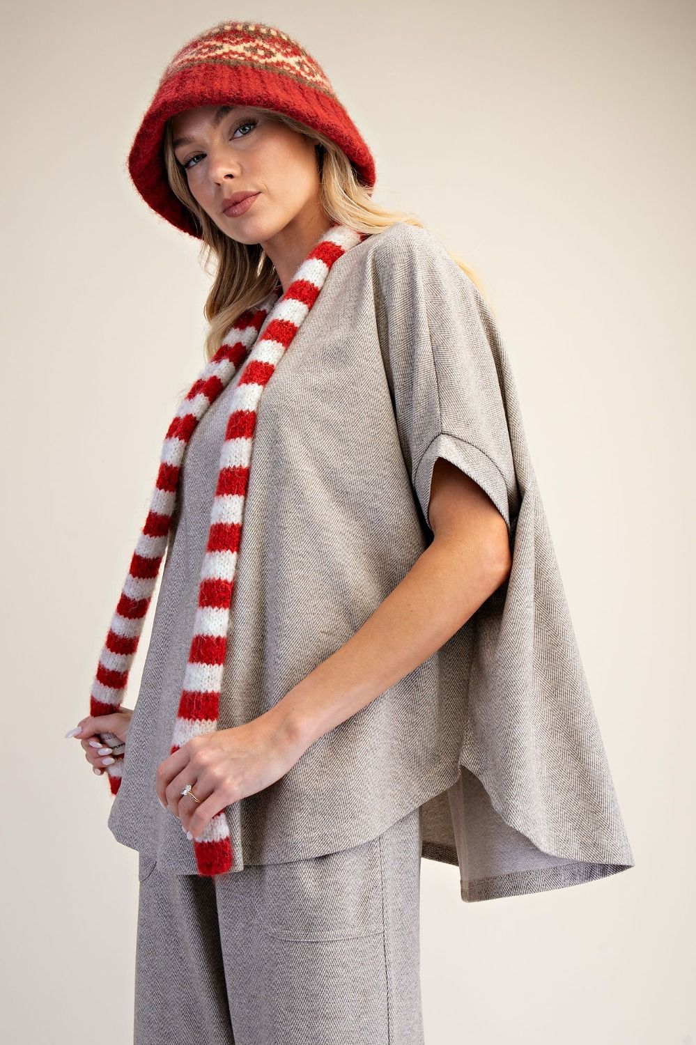Person wearing a red and white striped scarf, gray poncho, and patterned hat on a plain background