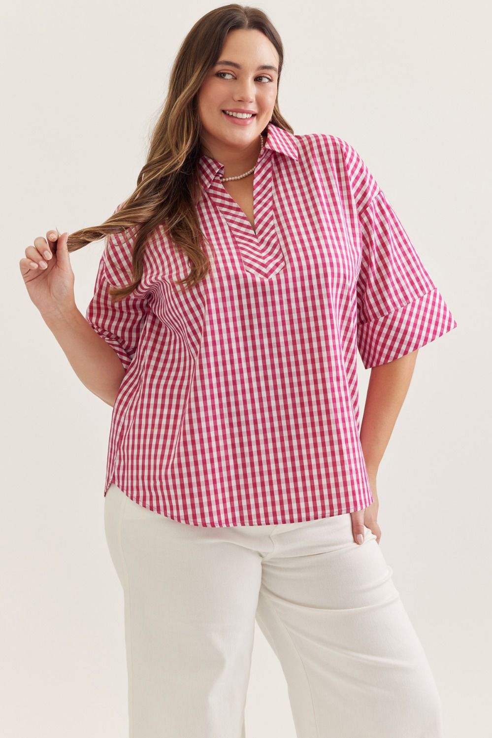 Woman wearing a red and white checkered shirt with white pants on a plain background