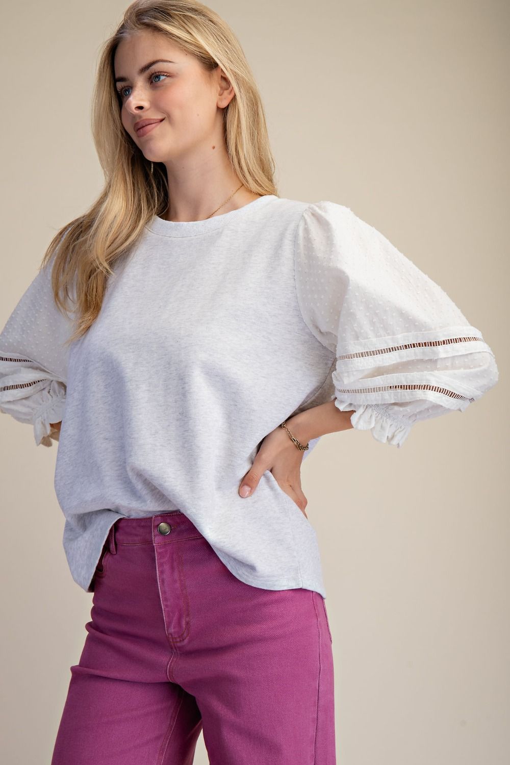 Woman wearing a white blouse with sheer sleeves and pink pants on a beige background