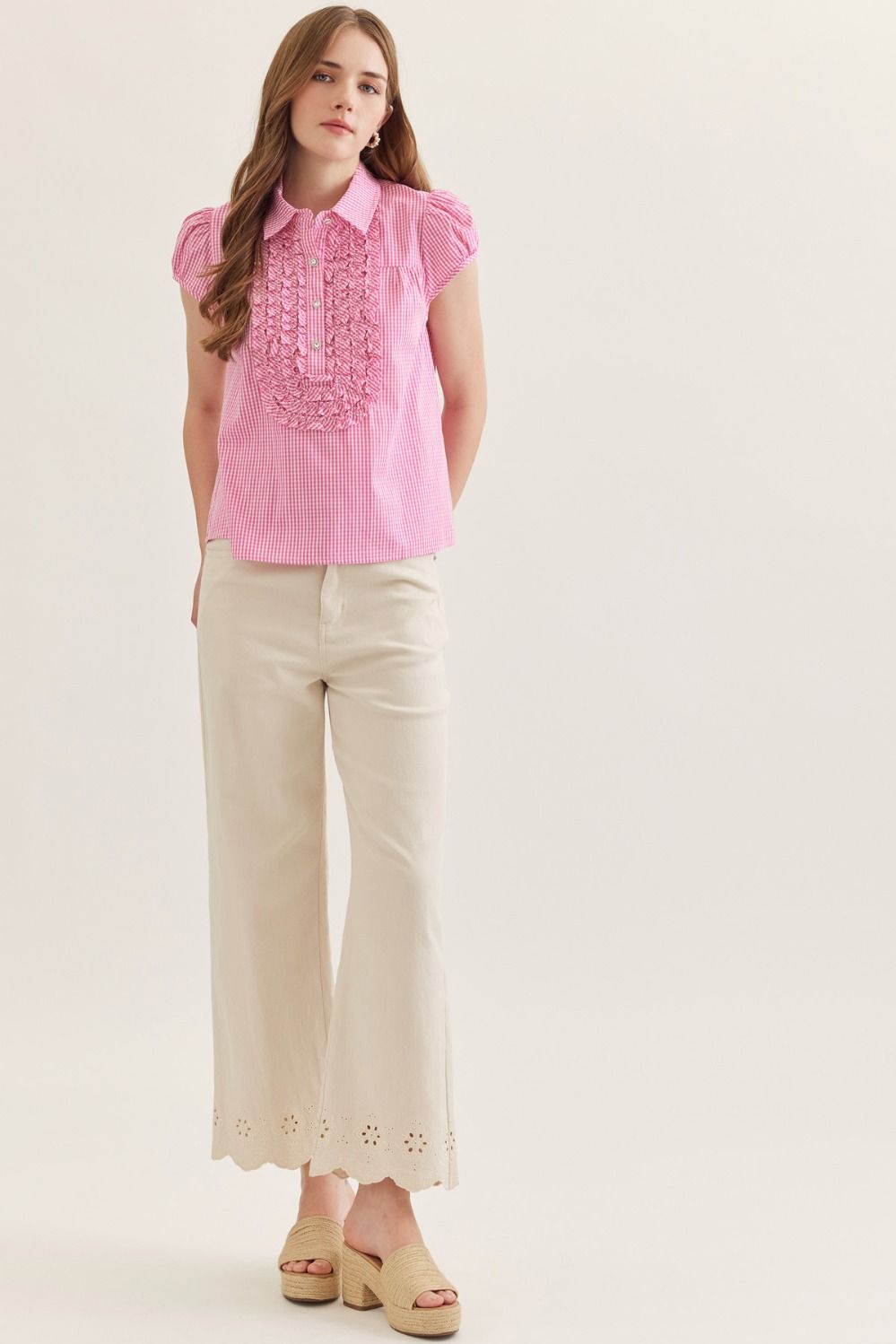 Woman wearing a pink blouse with lace details and beige pants on a white background