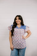Woman wearing a colorful patterned blouse against a light wooden panel background