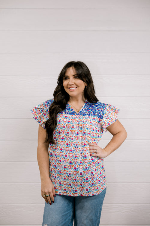 Woman wearing a colorful patterned blouse against a light wooden panel background
