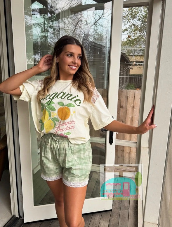 Woman wearing a 'organic' t-shirt with fruit graphics and green shorts, standing in front of a glass door.