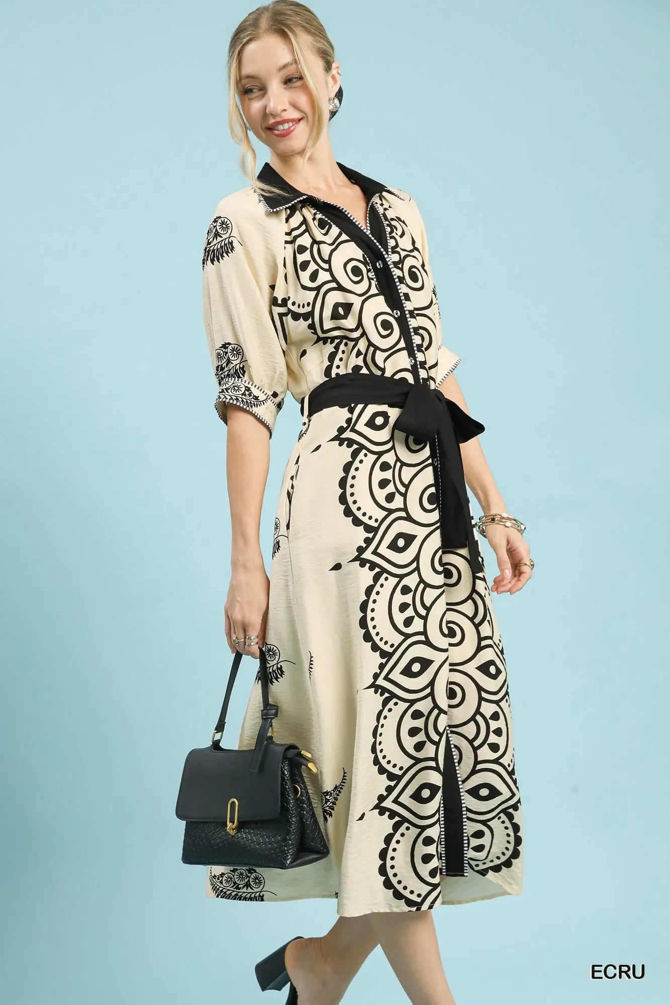 Woman wearing a patterned dress with a black belt against a light blue background