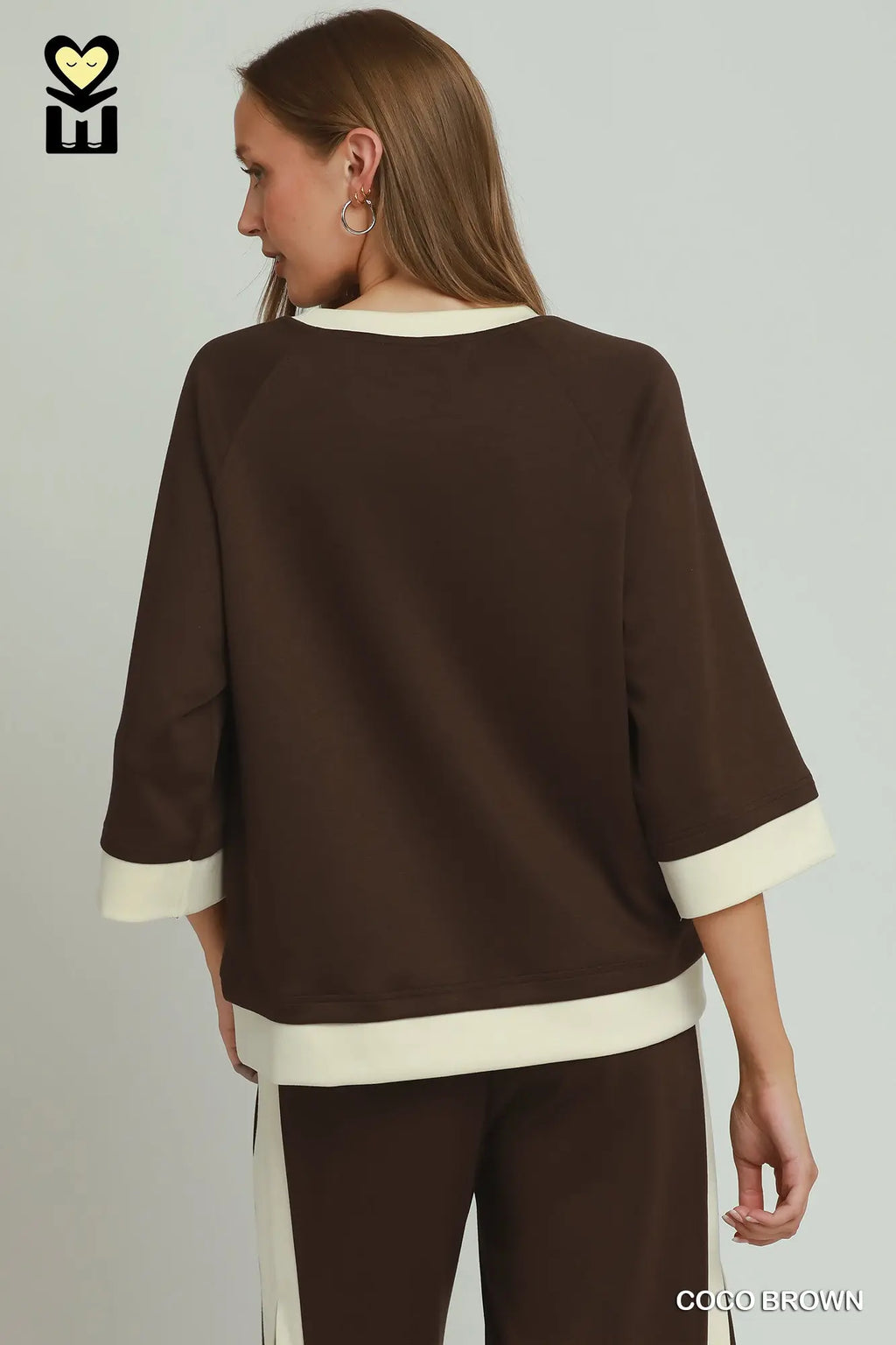 Woman wearing a brown outfit with white trim on a plain background