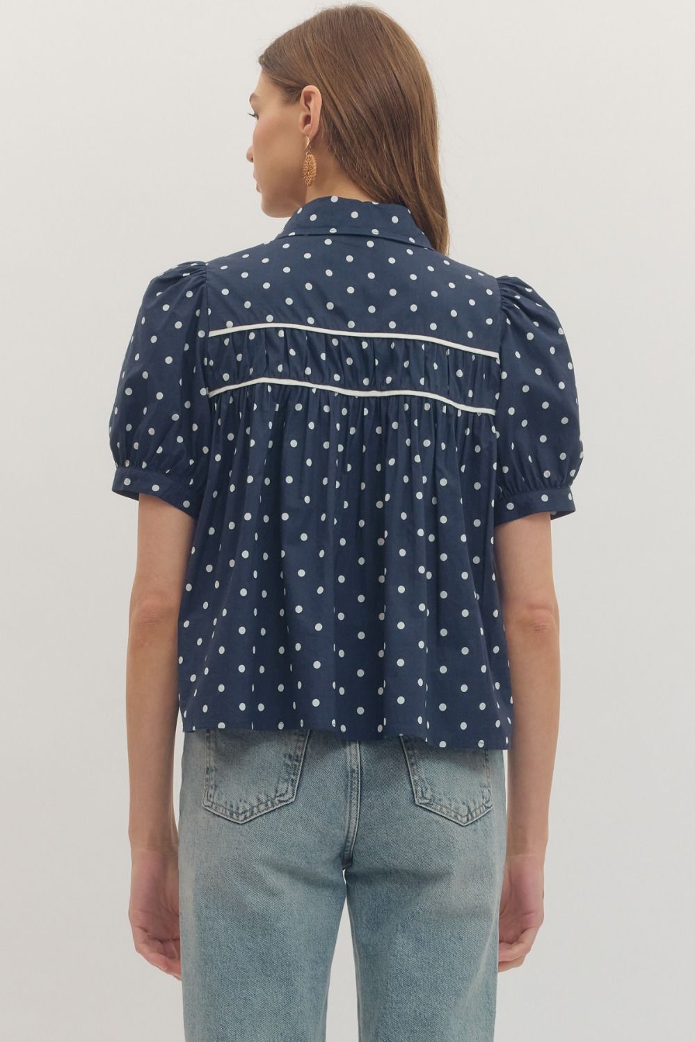 Person wearing a navy blue polka dot blouse with puff sleeves on a white background