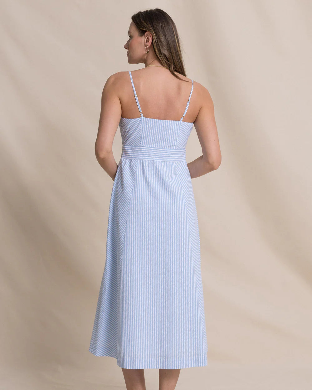 Woman wearing a light blue striped dress against a beige background