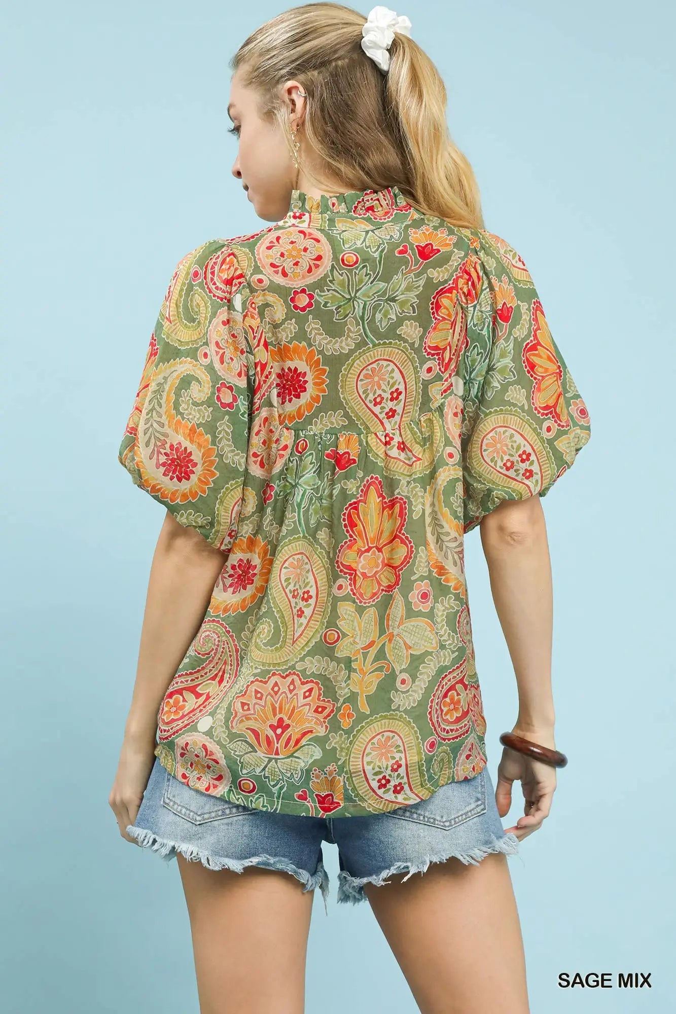 Woman wearing a colorful patterned blouse with denim shorts on a light blue background