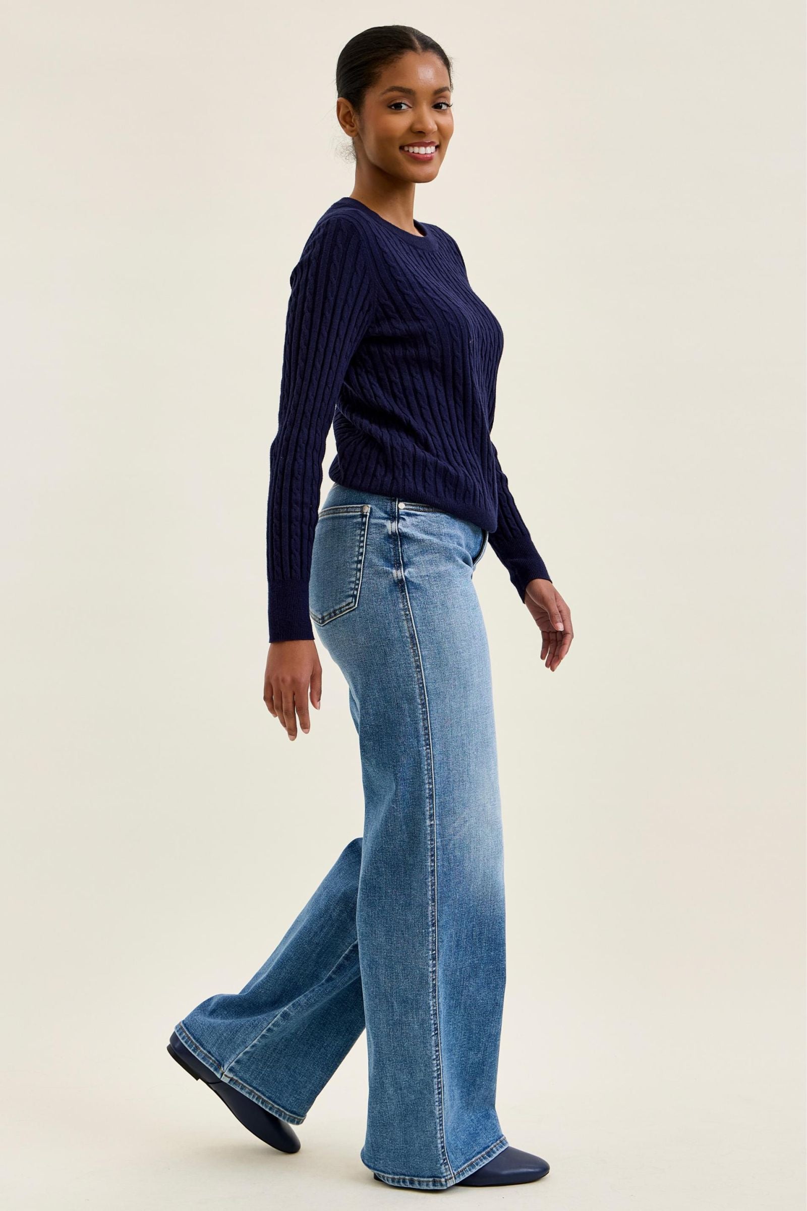 Woman wearing a navy sweater and blue jeans on a beige background