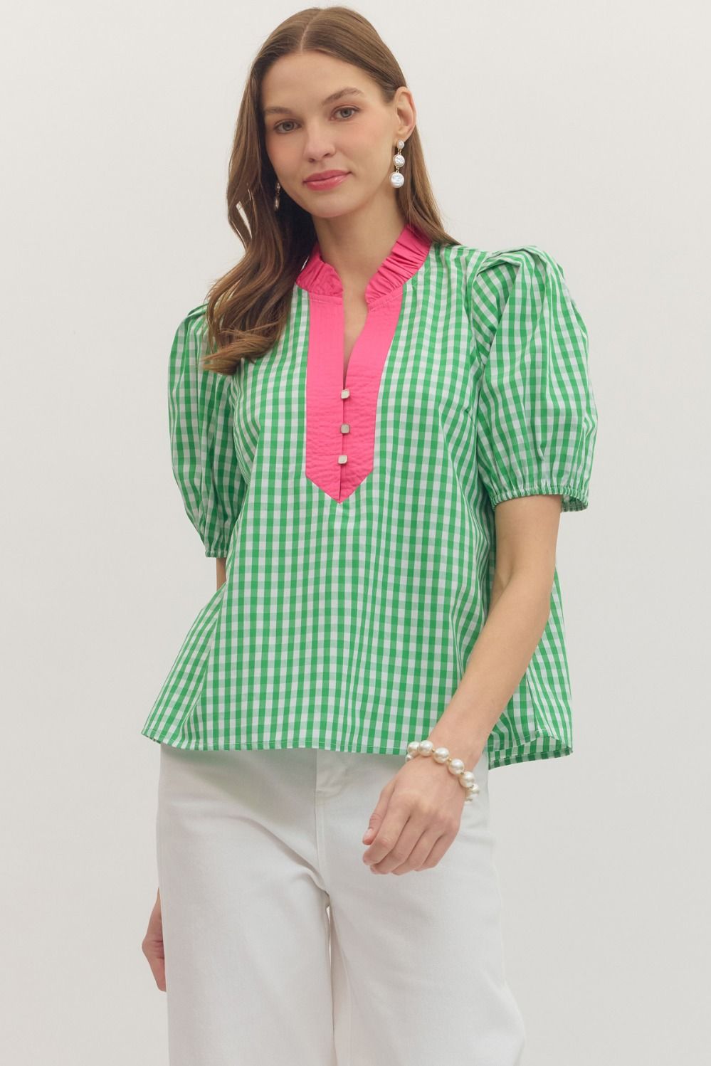 Woman wearing a green and pink checkered blouse with white pants on a plain background