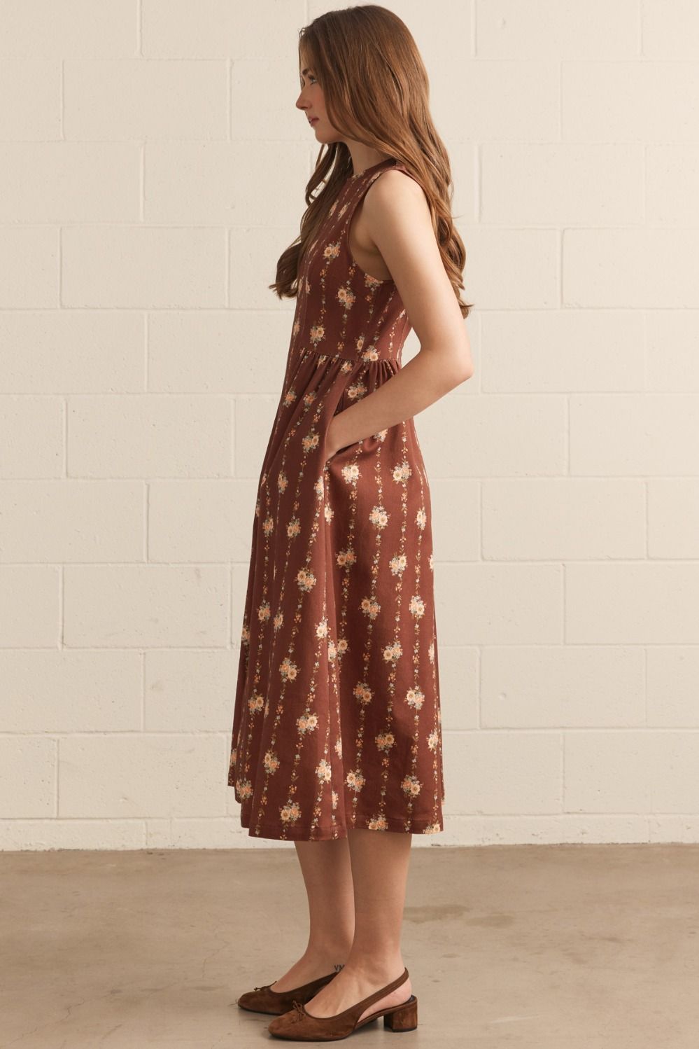 Woman wearing a patterned dress standing against a white tiled wall.