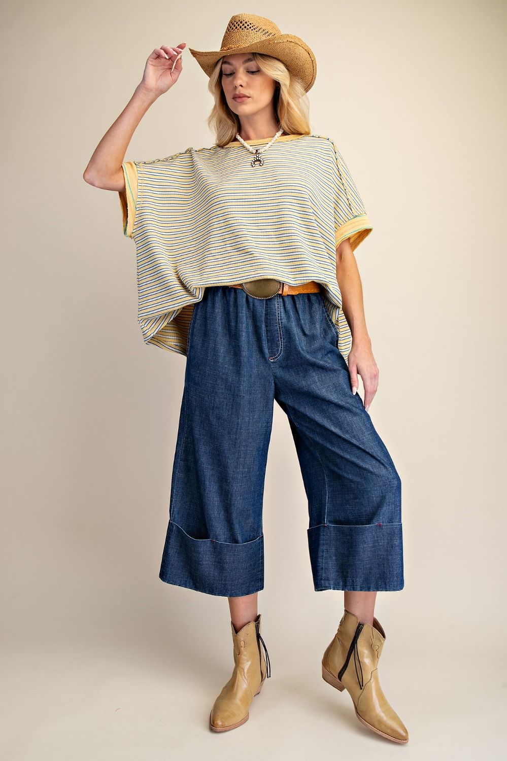 Woman wearing a striped top, wide-leg jeans, and a straw hat on a beige background