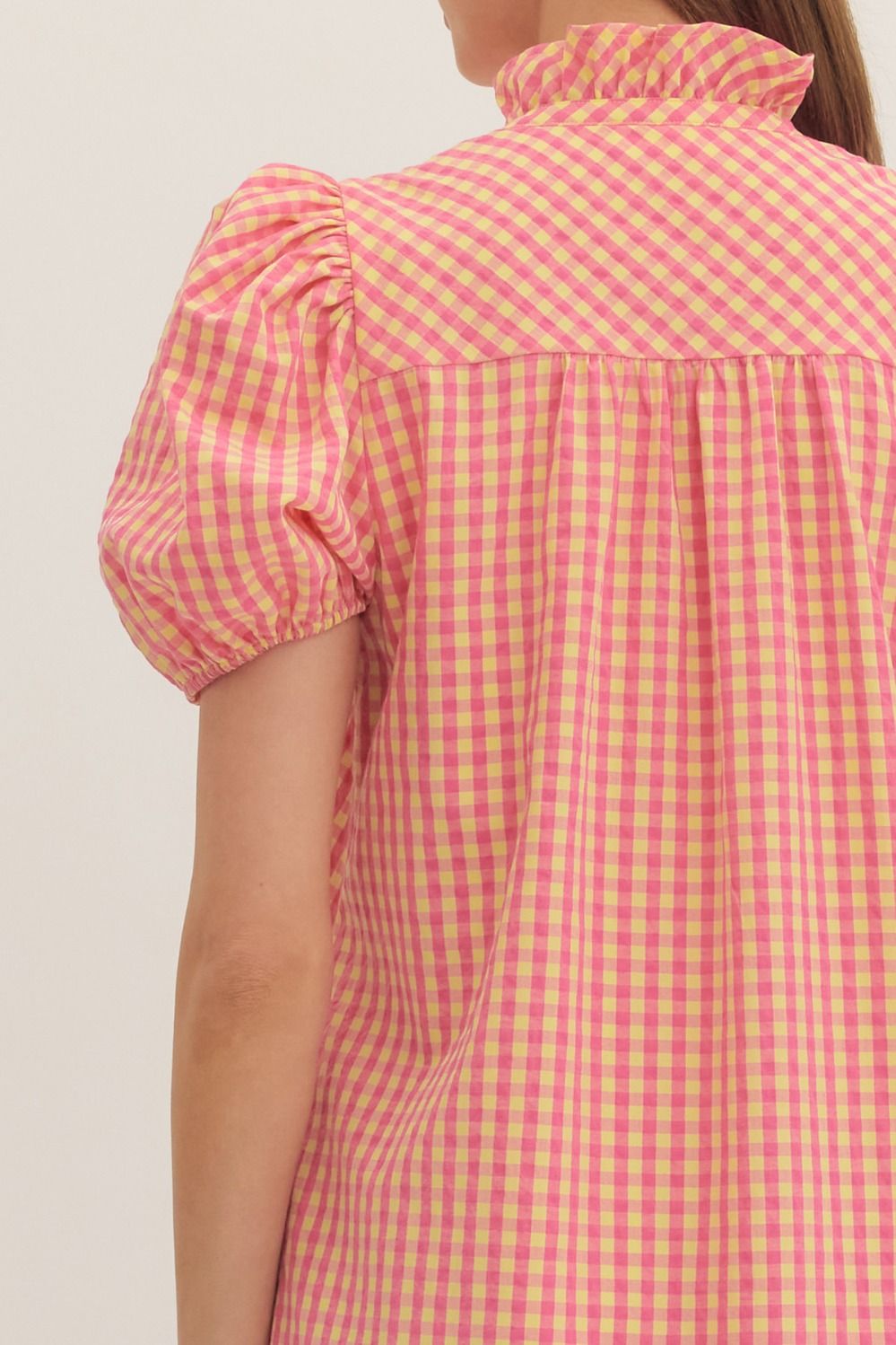 Person wearing a pink and yellow checkered dress with puff sleeves against a plain background
