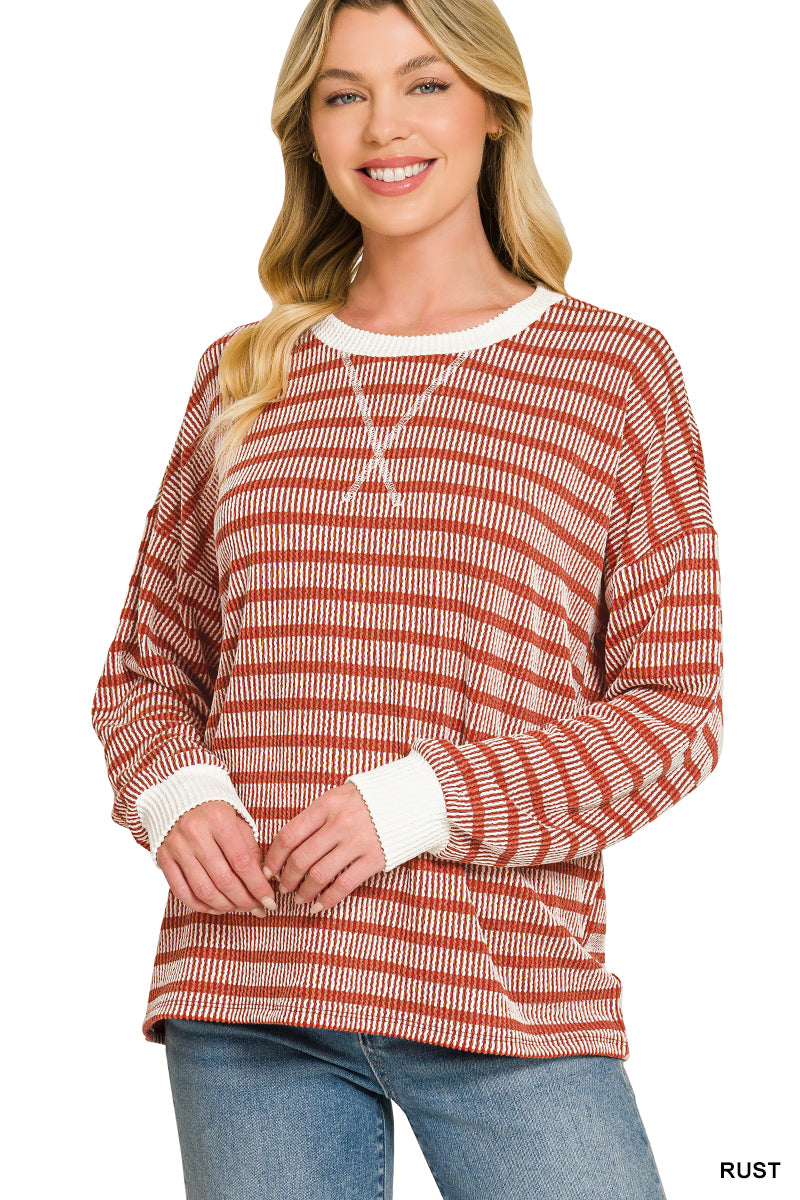 A woman wearing a rust and white striped long-sleeve knit top with white ribbed collar, cuffs, and hem, paired with blue jeans against a white background.