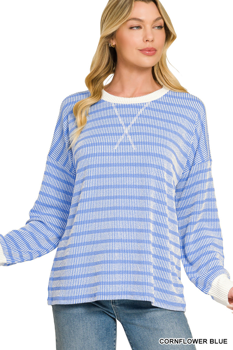 A woman wearing a long-sleeve knit top with horizontal cornflower blue and white stripes, paired with blue jeans, against a plain white background.