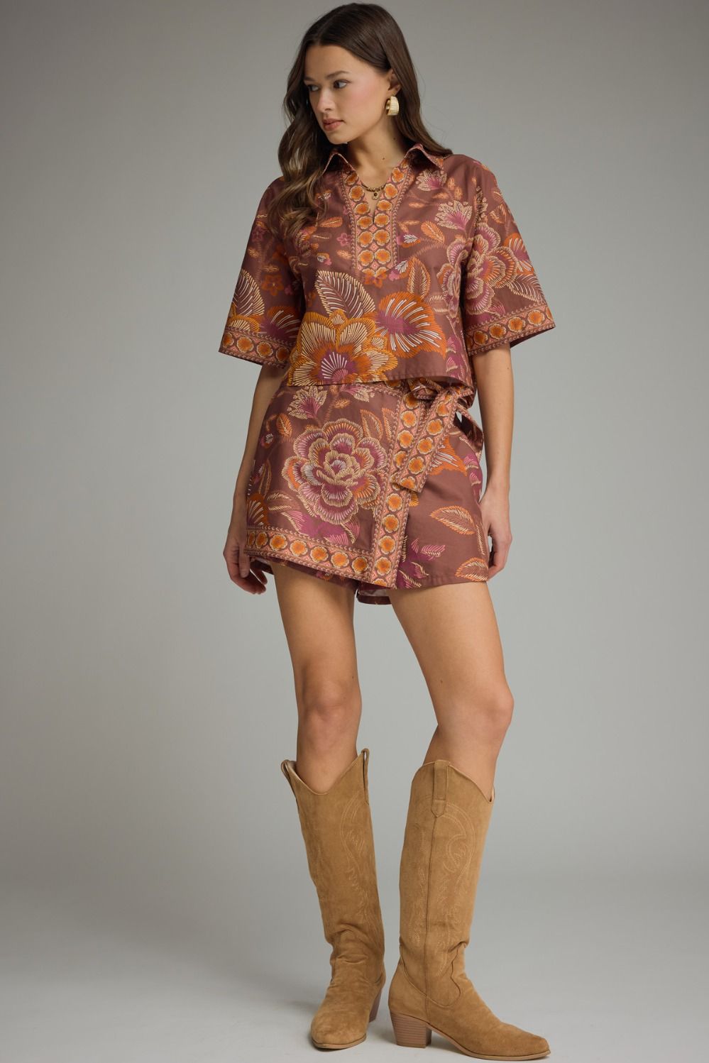Woman wearing a patterned dress and brown boots against a neutral background