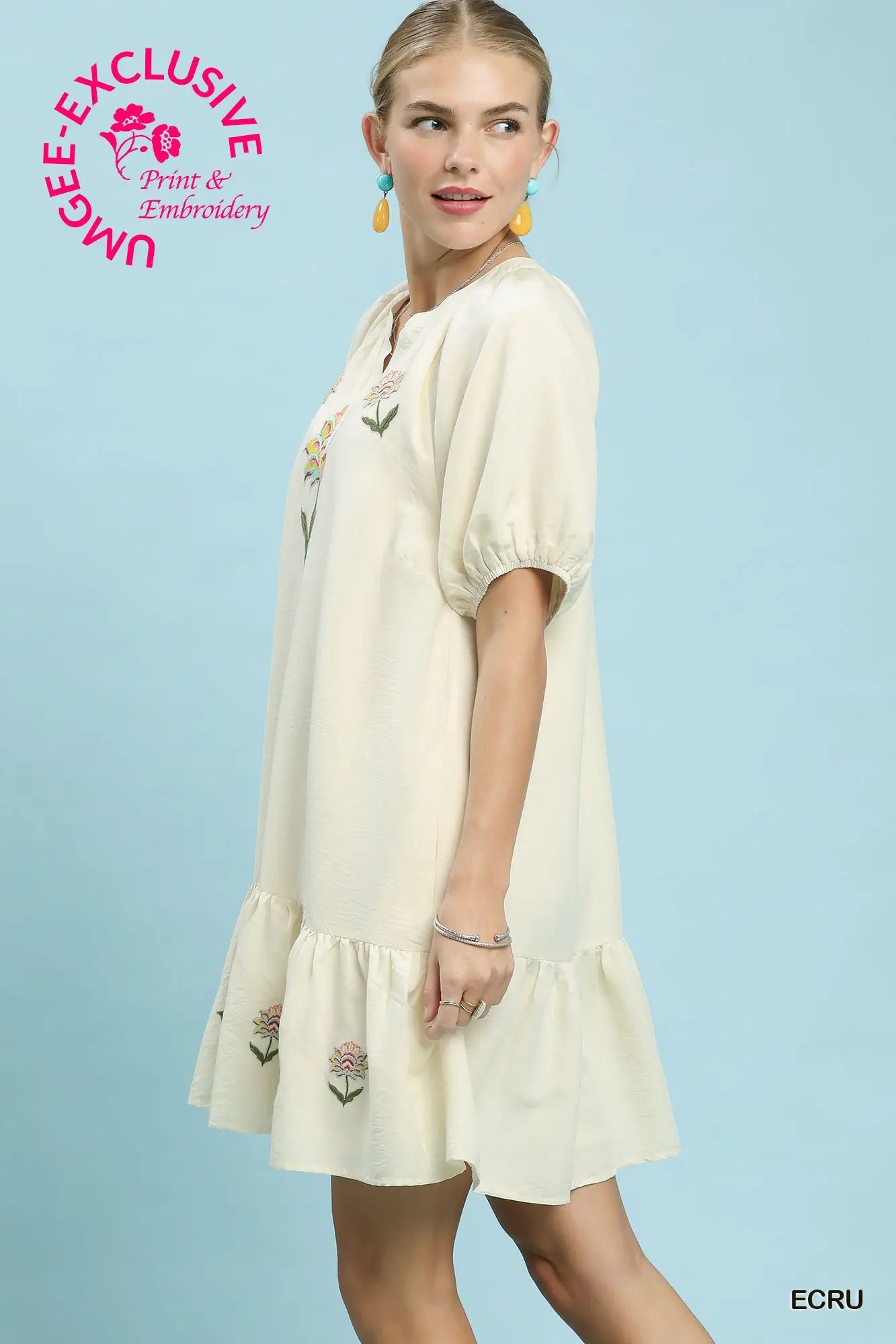 Woman wearing a cream-colored dress with floral embroidery against a light blue background