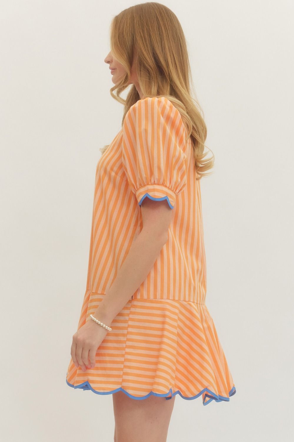 Woman wearing an orange and white striped dress with blue trim on a plain background