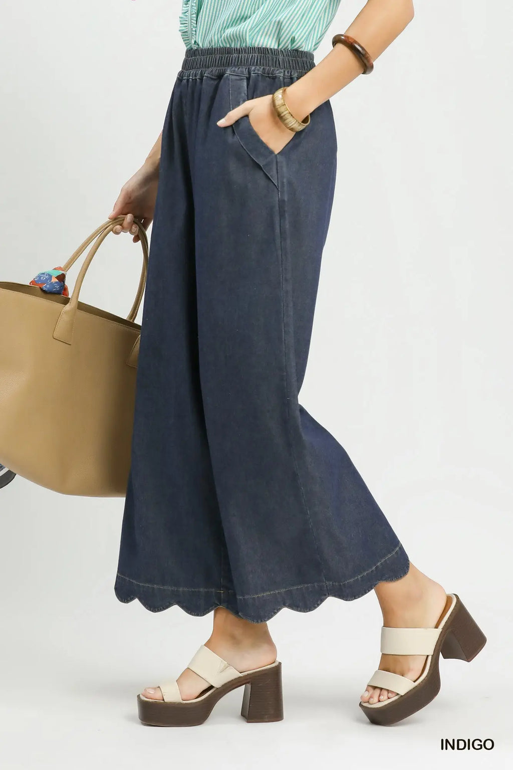 Person wearing navy wide-leg pants with a beige handbag on a white background