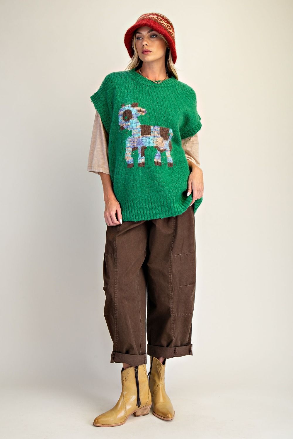 Person wearing a green sweater with a colorful animal design, brown pants, and yellow boots on a plain background