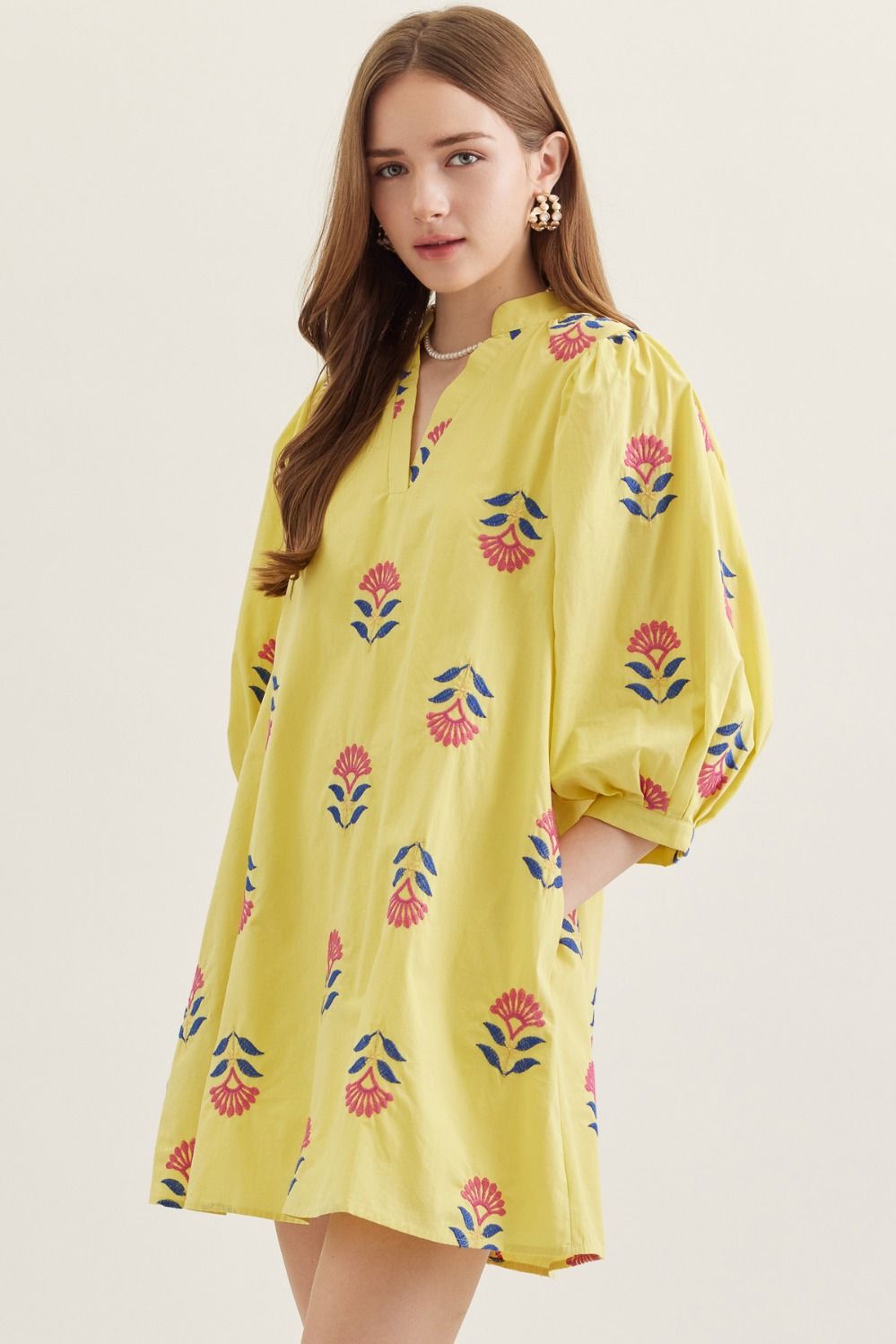 Woman wearing a yellow dress with floral patterns on a plain background