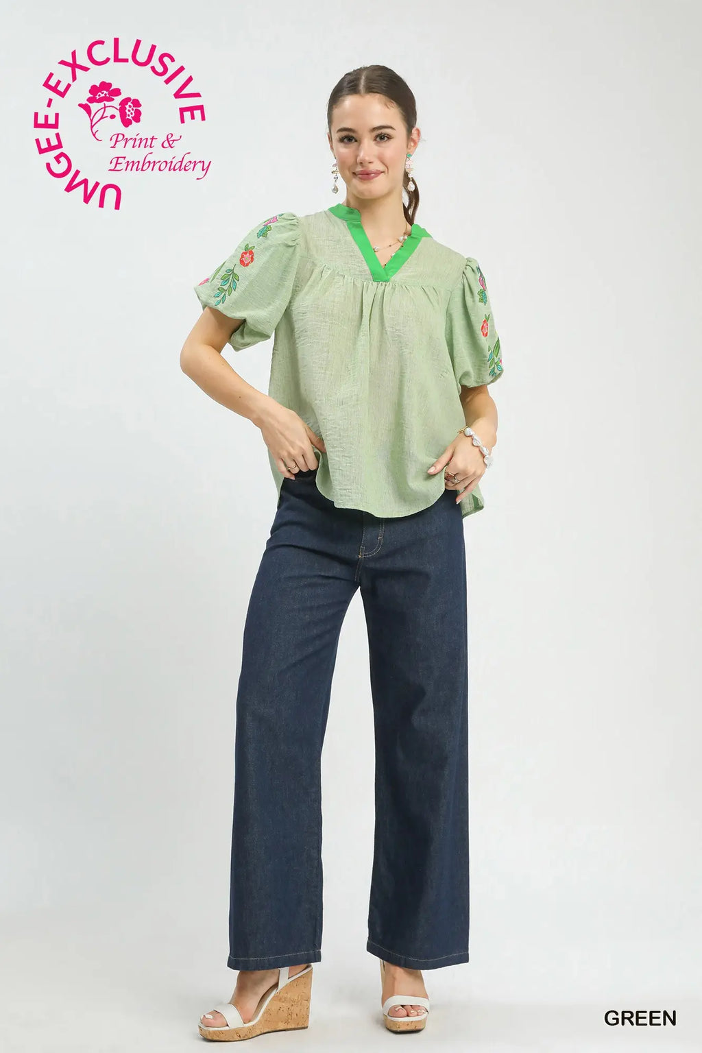 Woman wearing a green blouse with floral embroidery and dark jeans on a white background, with 'UMgee Exclusive' branding.