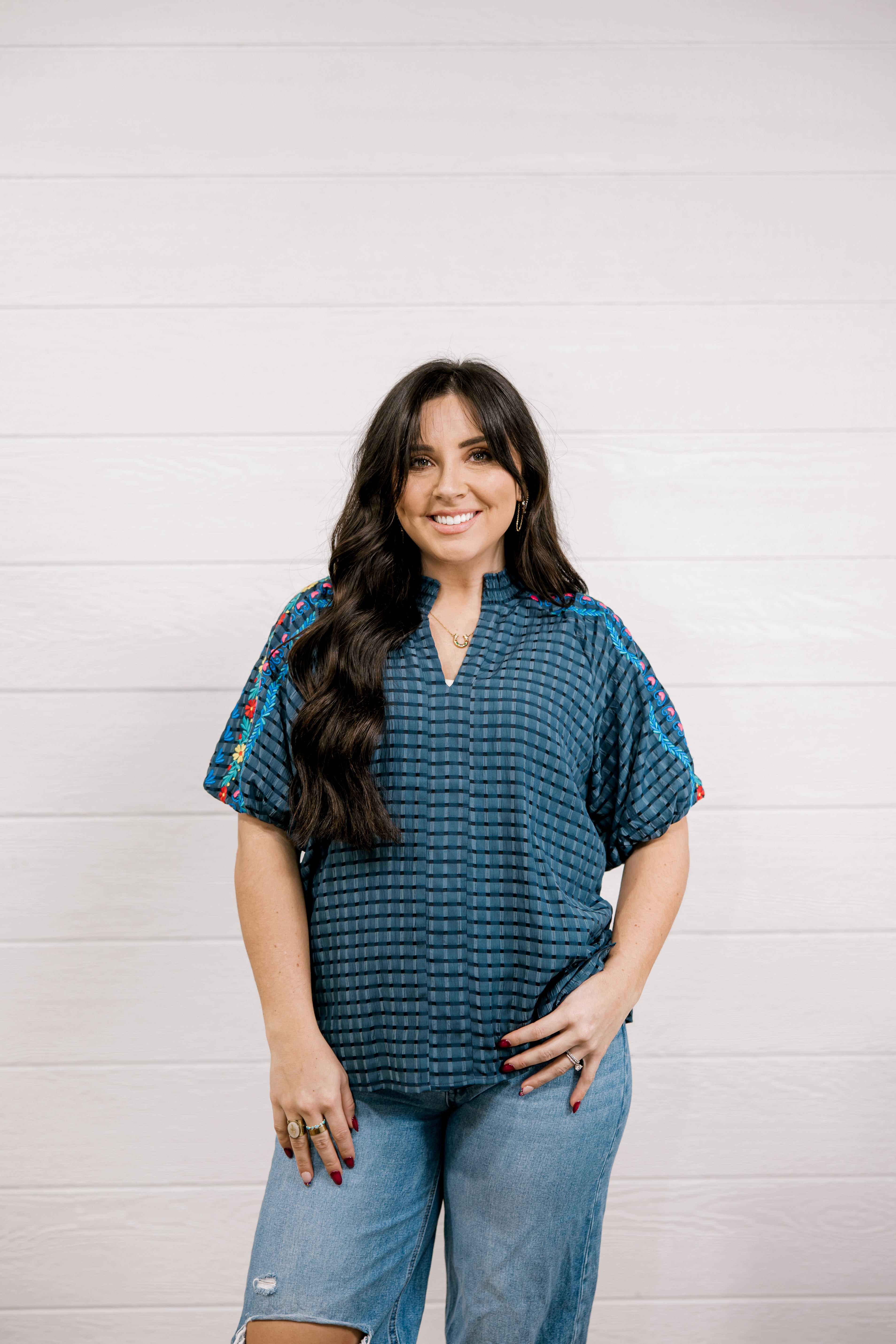 Woman wearing a blue patterned top and jeans against a white background