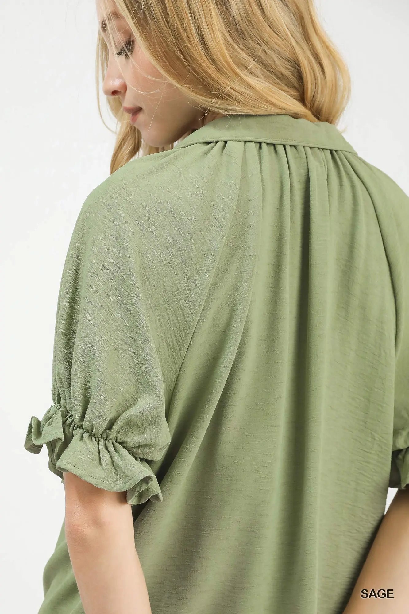 Woman wearing a green blouse with ruffled sleeves on a white background