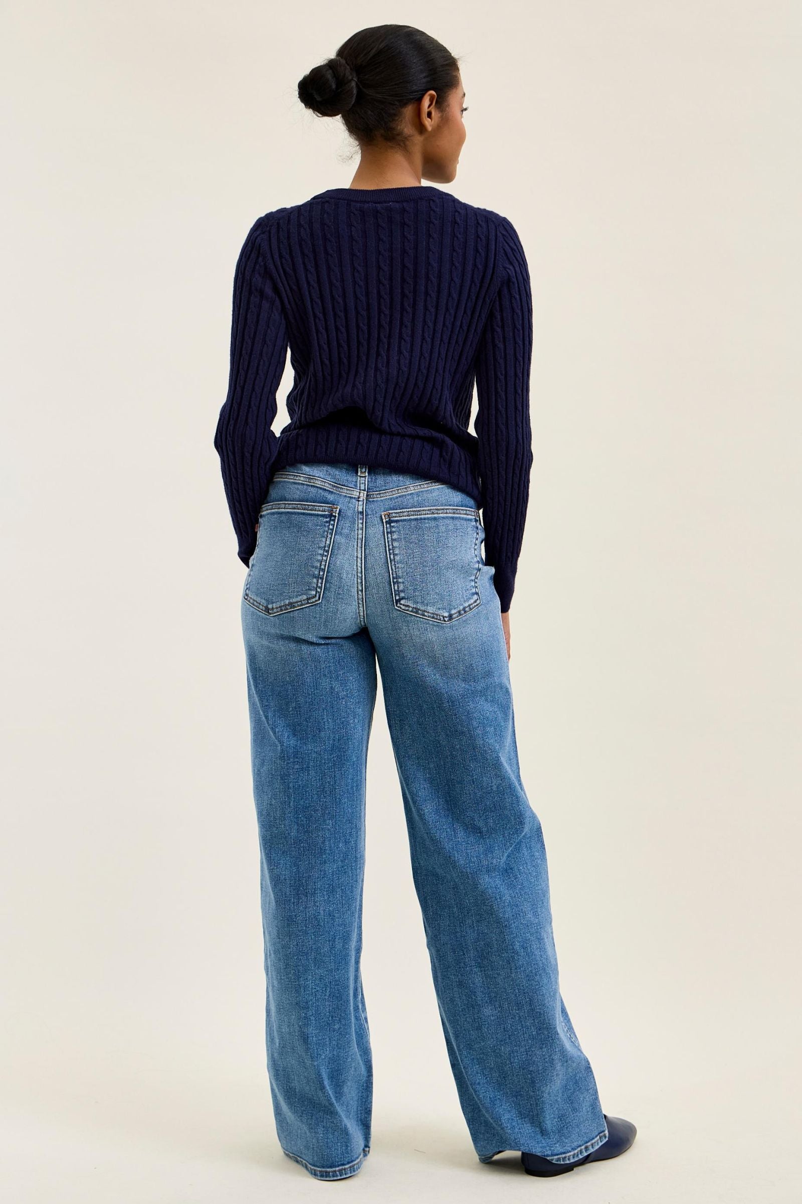 Person wearing a navy sweater and blue jeans on a plain background
