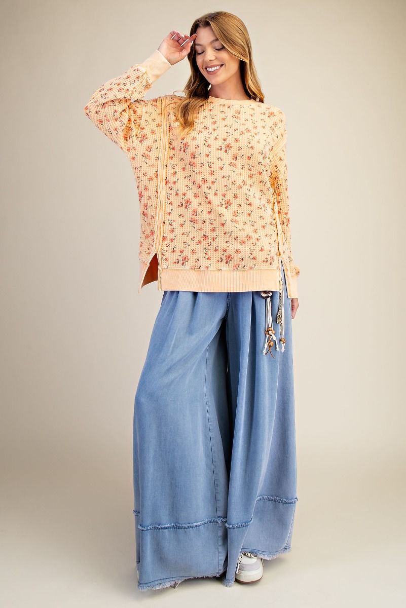 Woman wearing a floral blouse and blue pants against a beige background