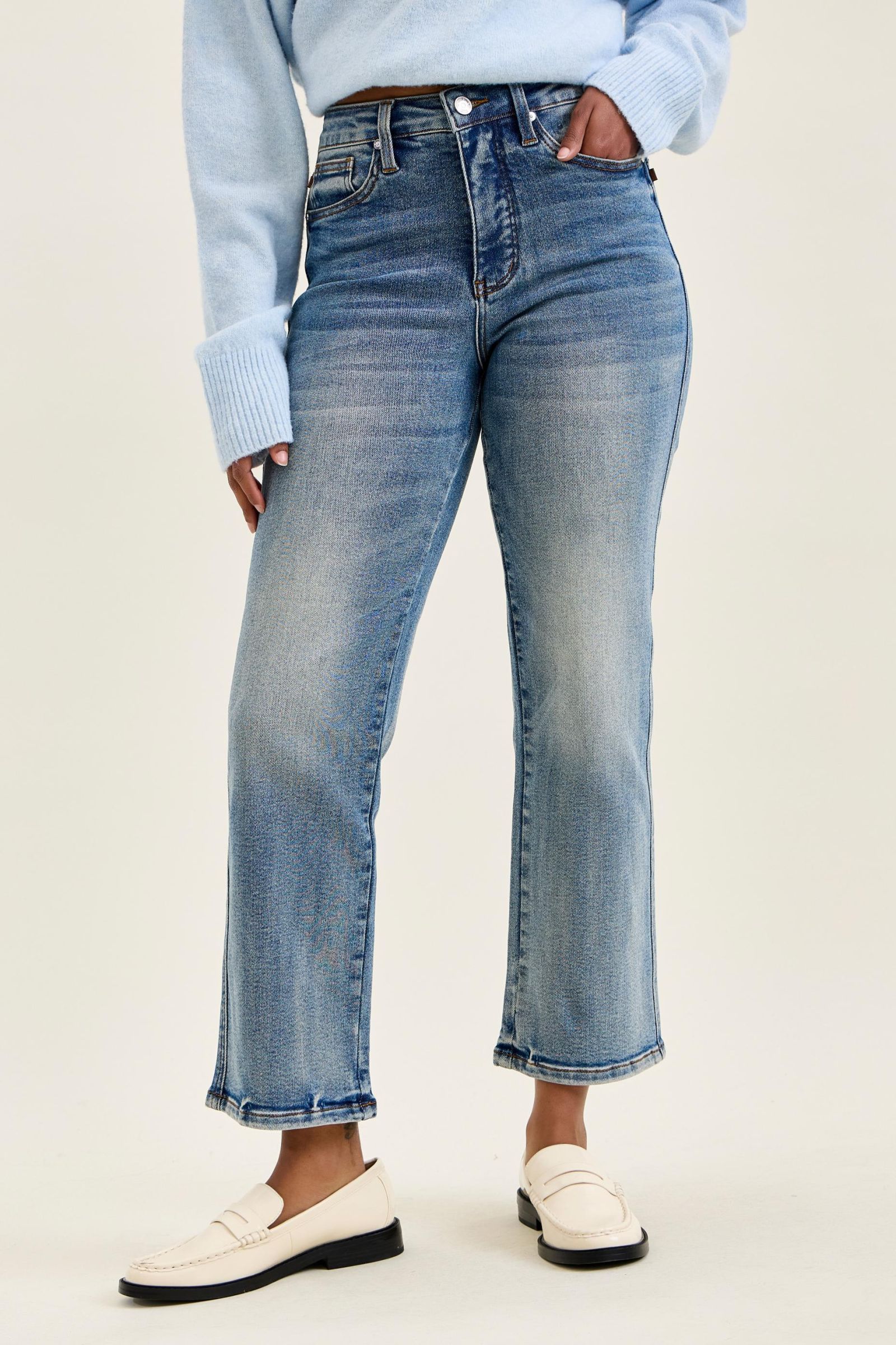 Person wearing blue jeans and a light blue sweater on a plain background