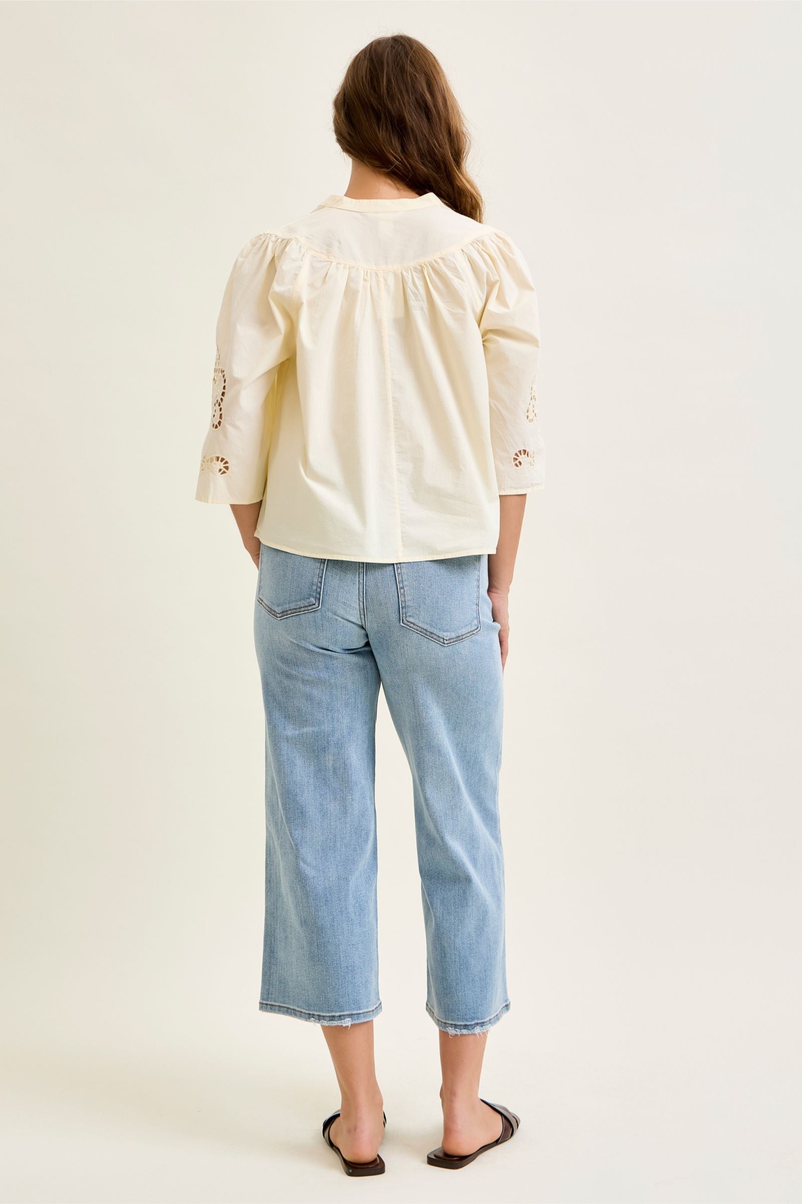 Person wearing a cream blouse and light blue jeans on a plain background