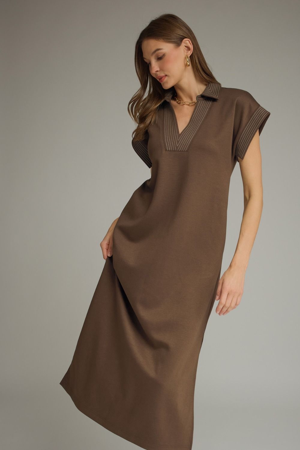 Woman wearing a brown dress with a collar against a gray background