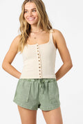 Woman wearing a cream tank top with buttons and green shorts on a white background