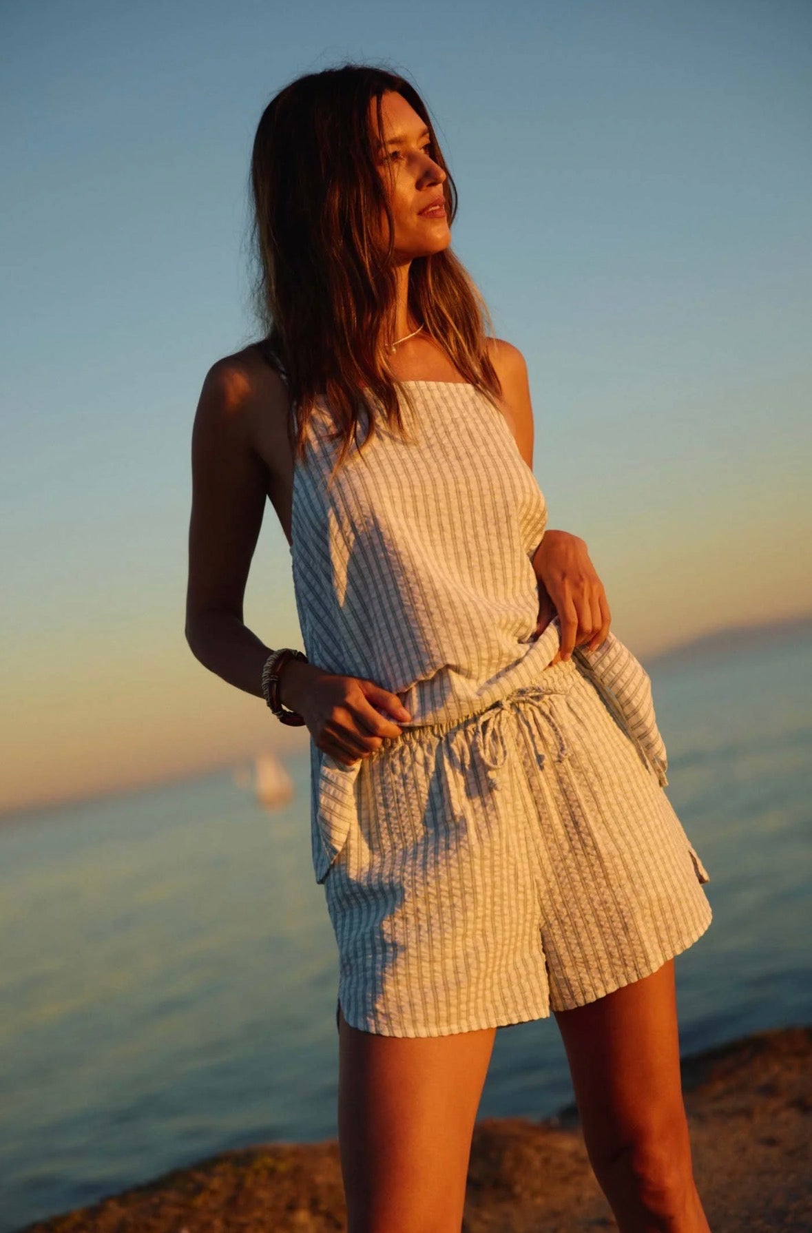 Woman in a white dress standing by the water at sunset