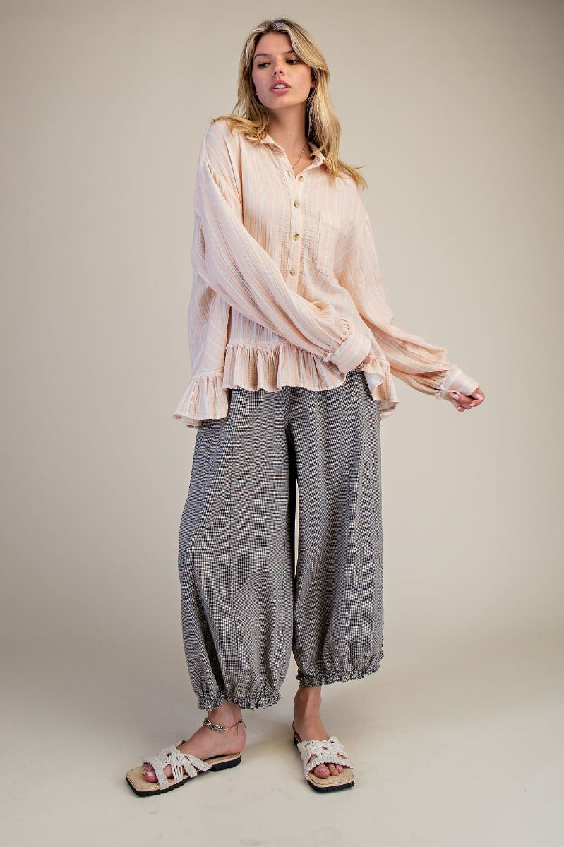 Woman wearing a light pink blouse and gray patterned pants on a beige background