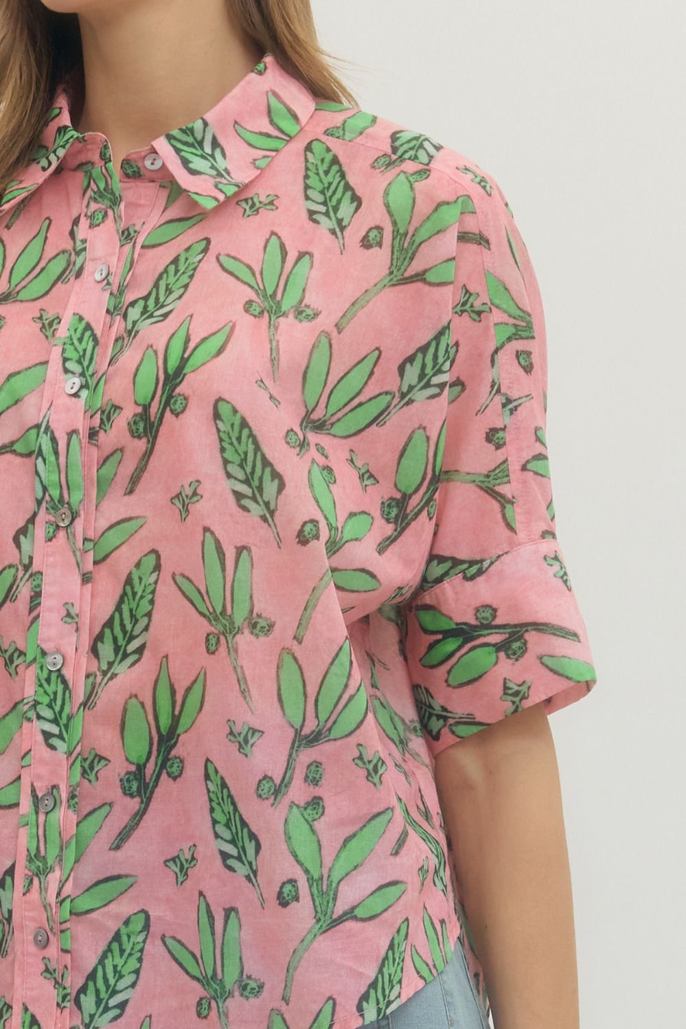Person wearing a pink shirt with green leaf pattern on a plain background