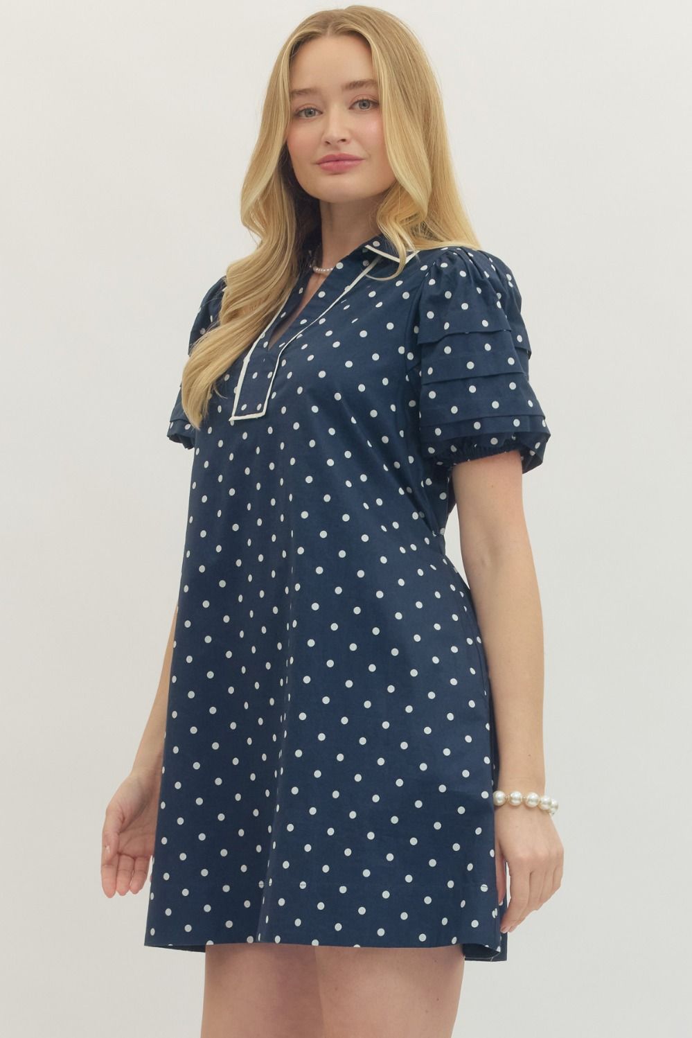 Woman wearing a navy blue dress with white polka dots against a plain background