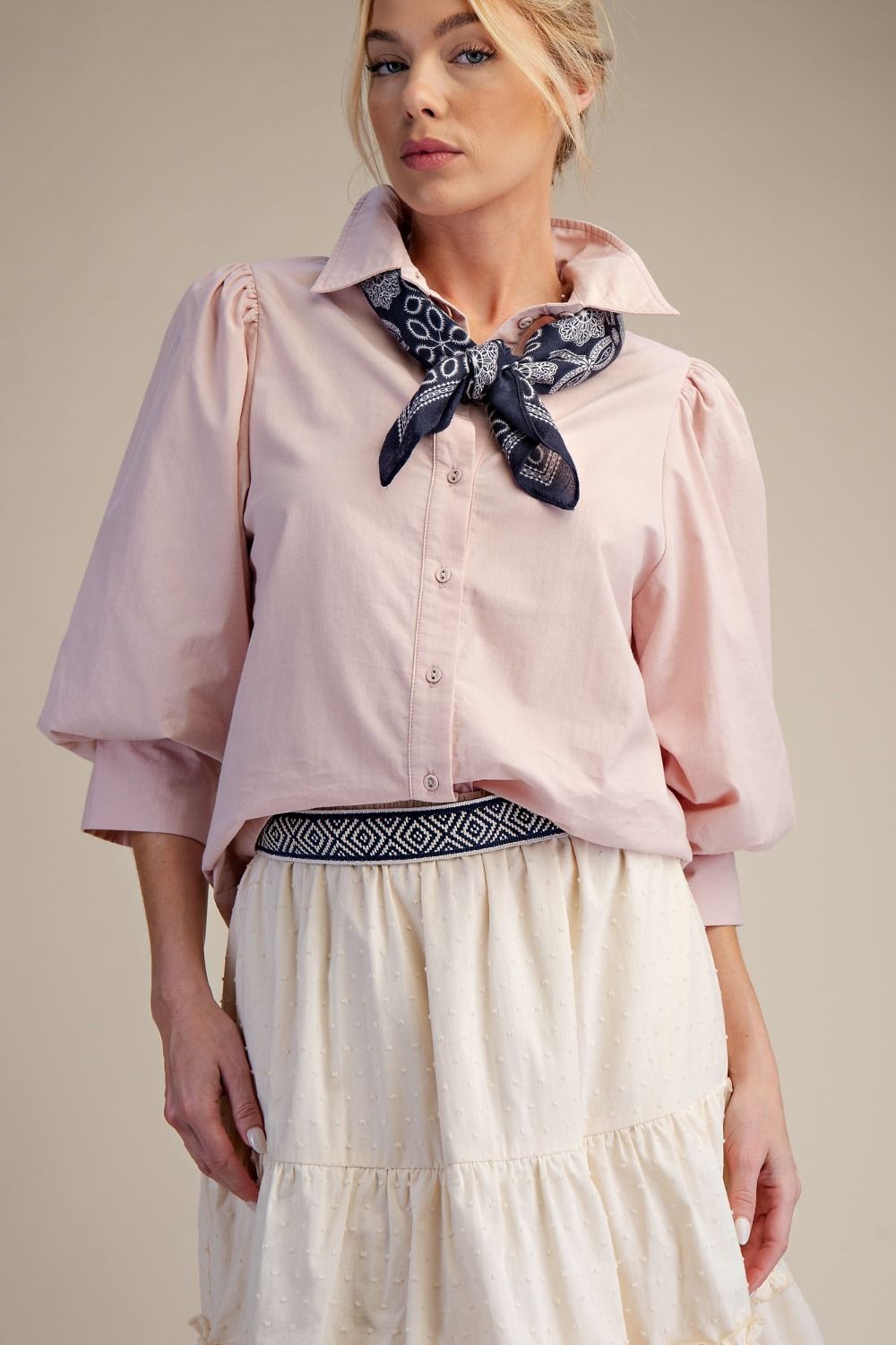 Woman wearing a pink blouse with a black and white patterned scarf around her neck against a beige background